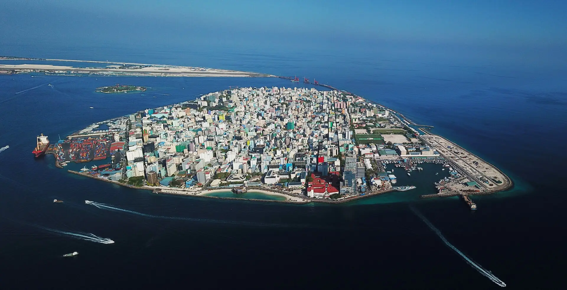 Aerial view of Malé surrounded by reef, with harbour berths and vessel traffic in the channel.