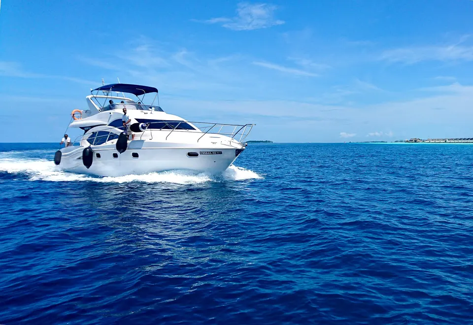 Yacht under way in open Maldivian water with a low island on the horizon.