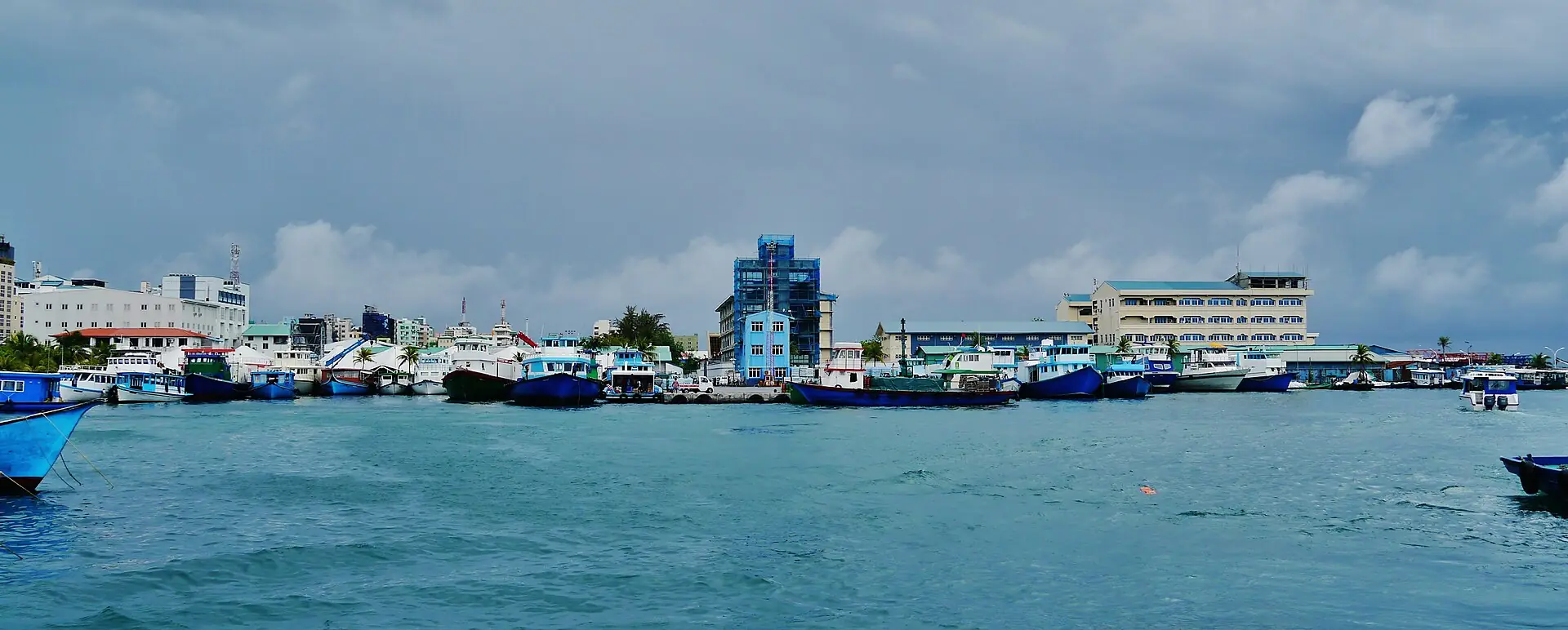 Working vessels moored along the south west harbour at Malé, with the island waterfront behind.